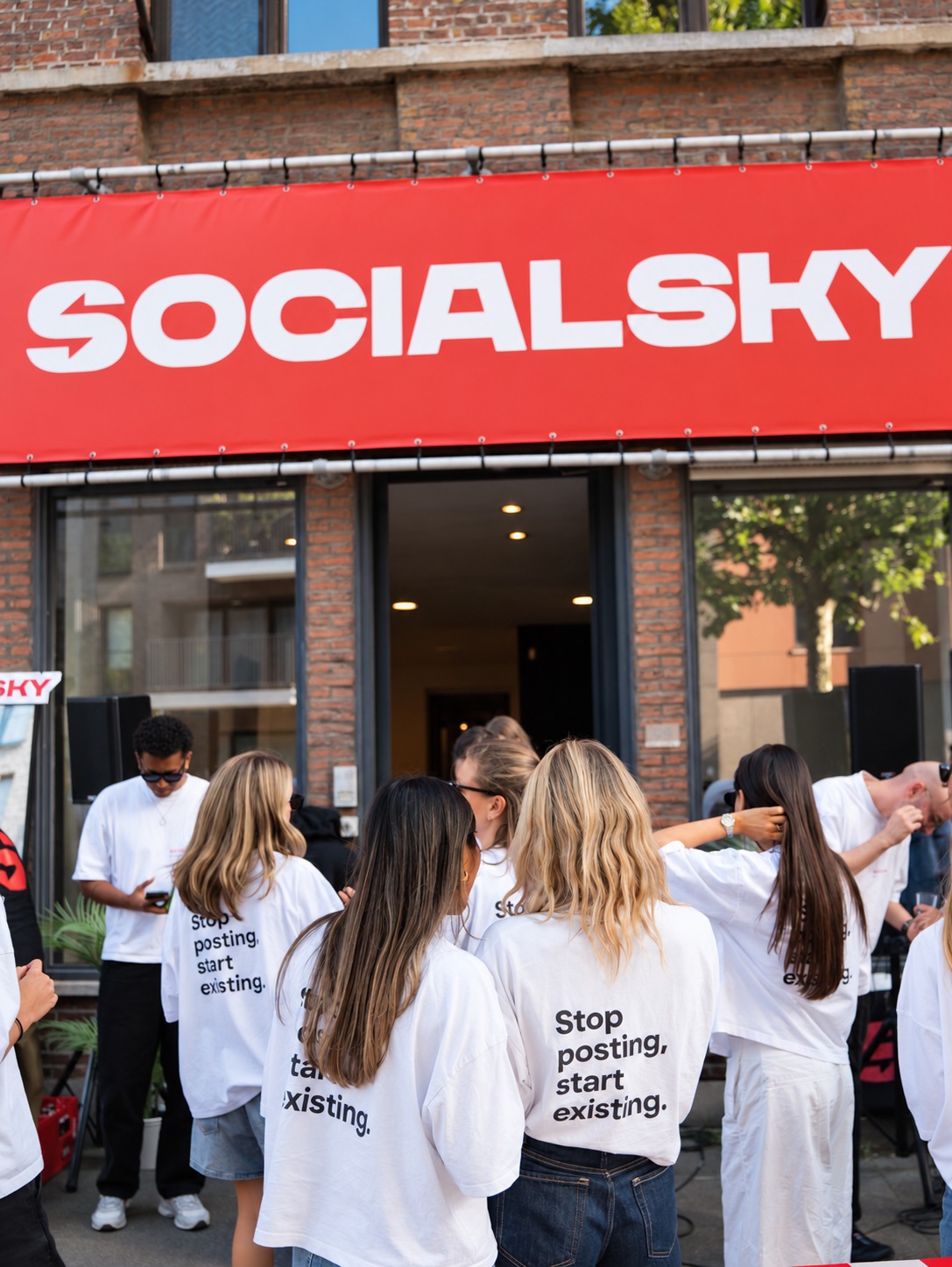 Groupe en t-shirts blancs rassemblé devant une façade en briques sous une banderole rouge